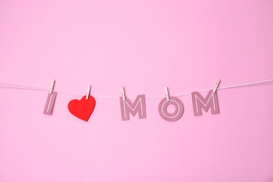 Phrase "I LOVE MOM" made of paper letters hanging on rope against color background. Happy Mother's Day