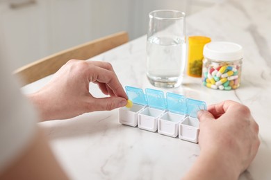 Woman with pills, organizer and glass of water at white marble table, closeup