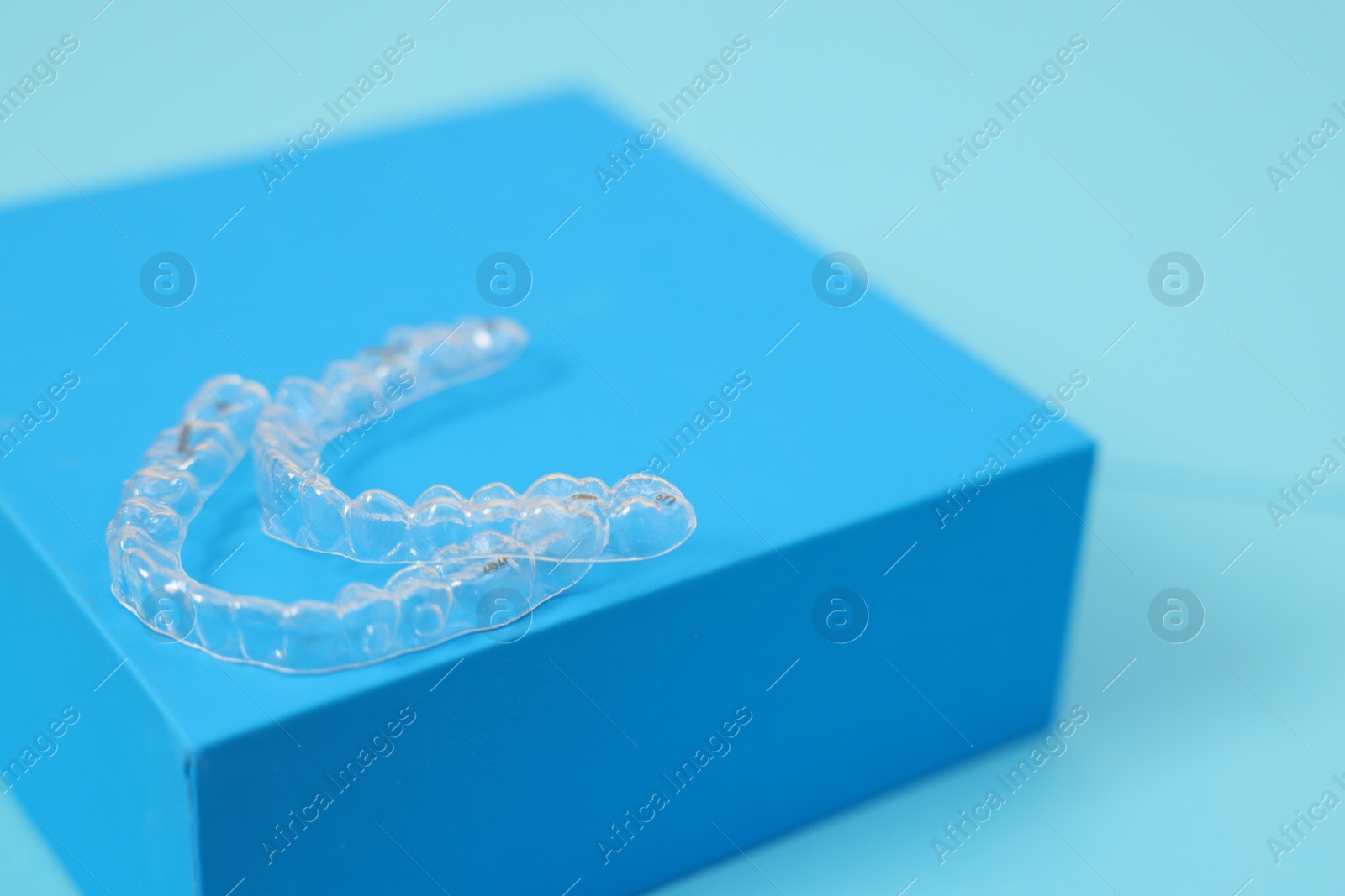 Photo of Transparent dental aligners on light blue background, closeup. Space for text