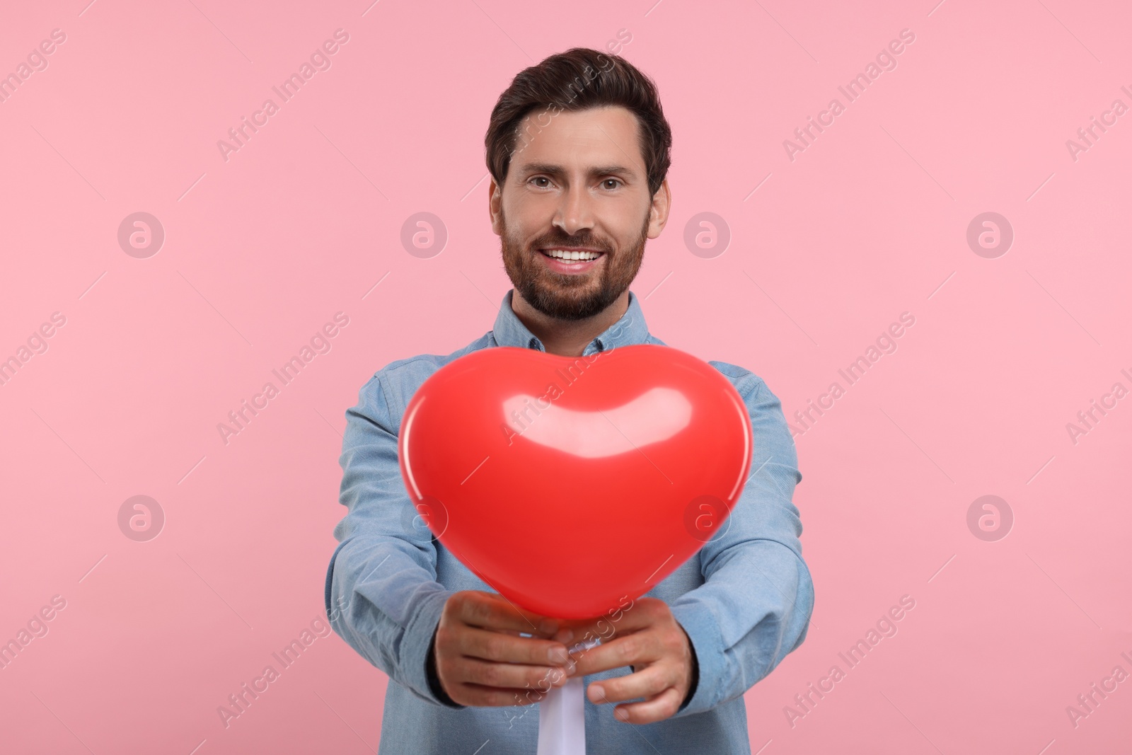 Photo of Happy man holding red heart shaped balloon on pink background