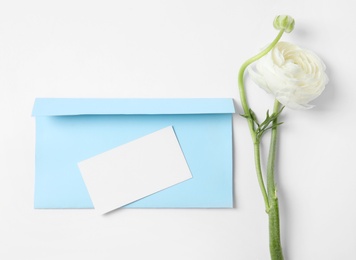 Photo of Envelope with card and beautiful ranunculus flower on white background, top view. Space for text