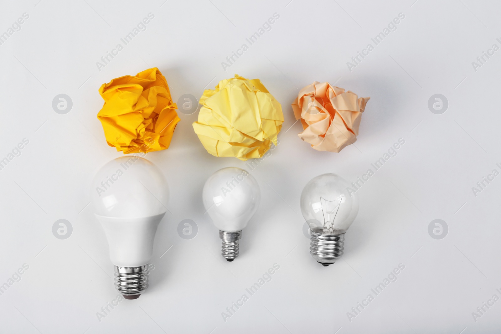 Photo of Composition with lamp bulbs and crumpled paper balls on white background, top view. Creative concept