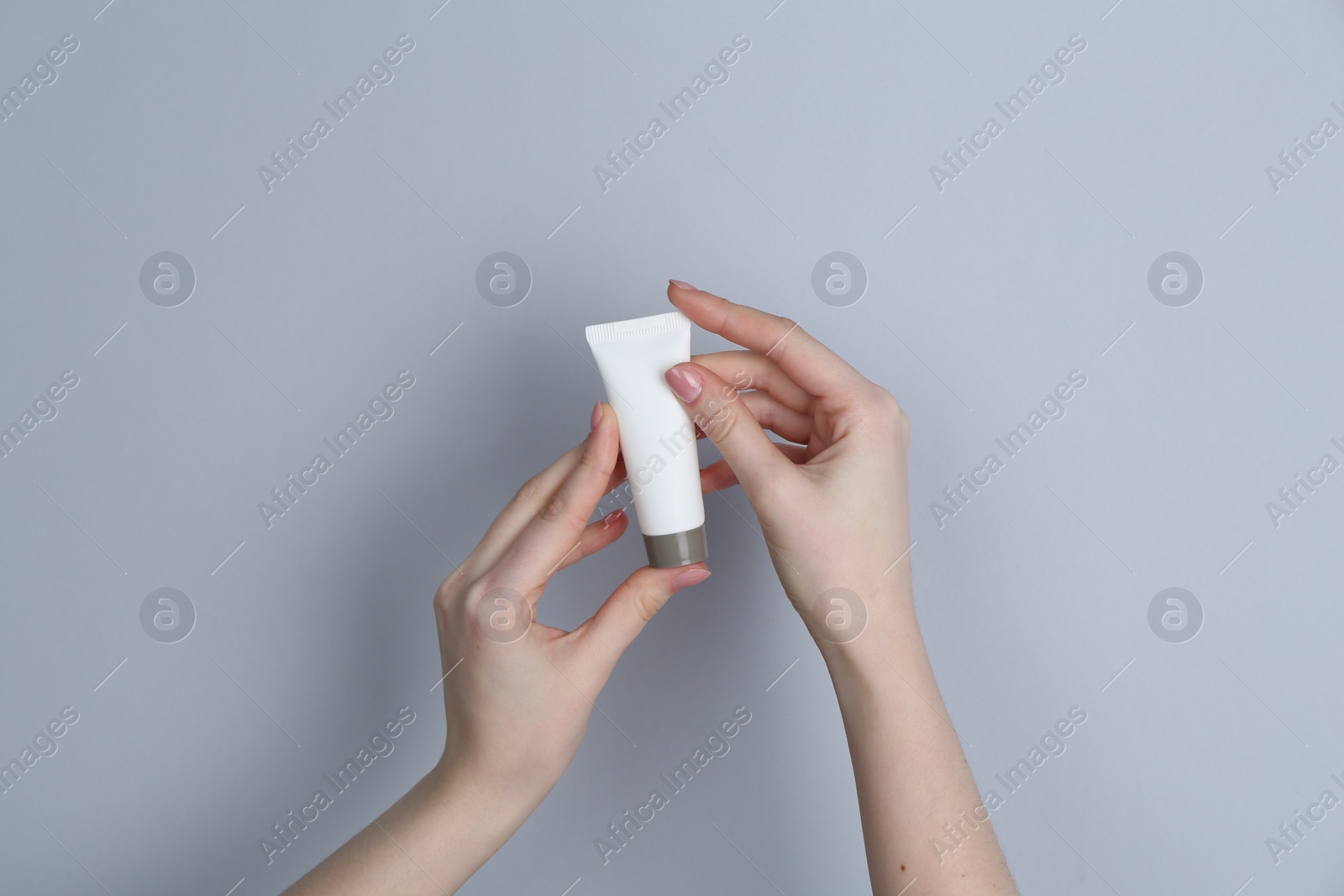 Photo of Woman holding tube of cream on grey background, closeup