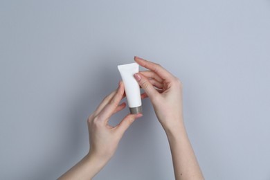 Woman holding tube of cream on grey background, closeup