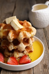 Delicious Belgian waffles with honey, butter and strawberries on wooden table, closeup