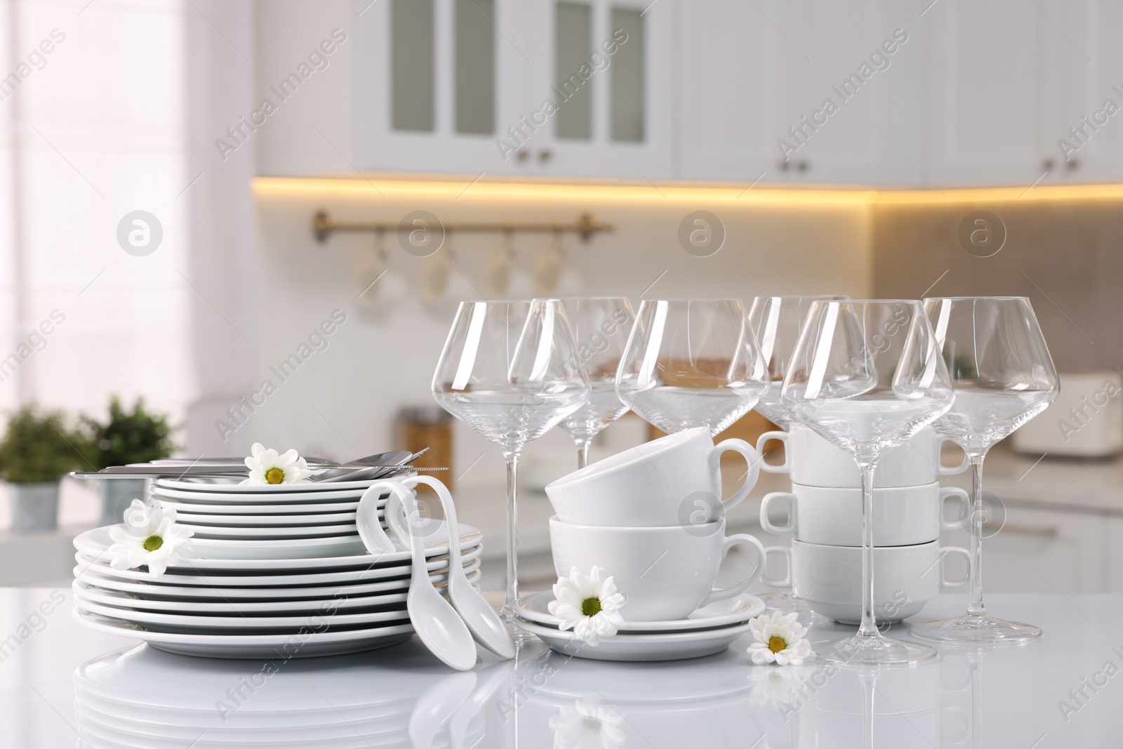 Photo of Set of clean dishware, glasses, cutlery and flowers on table in kitchen