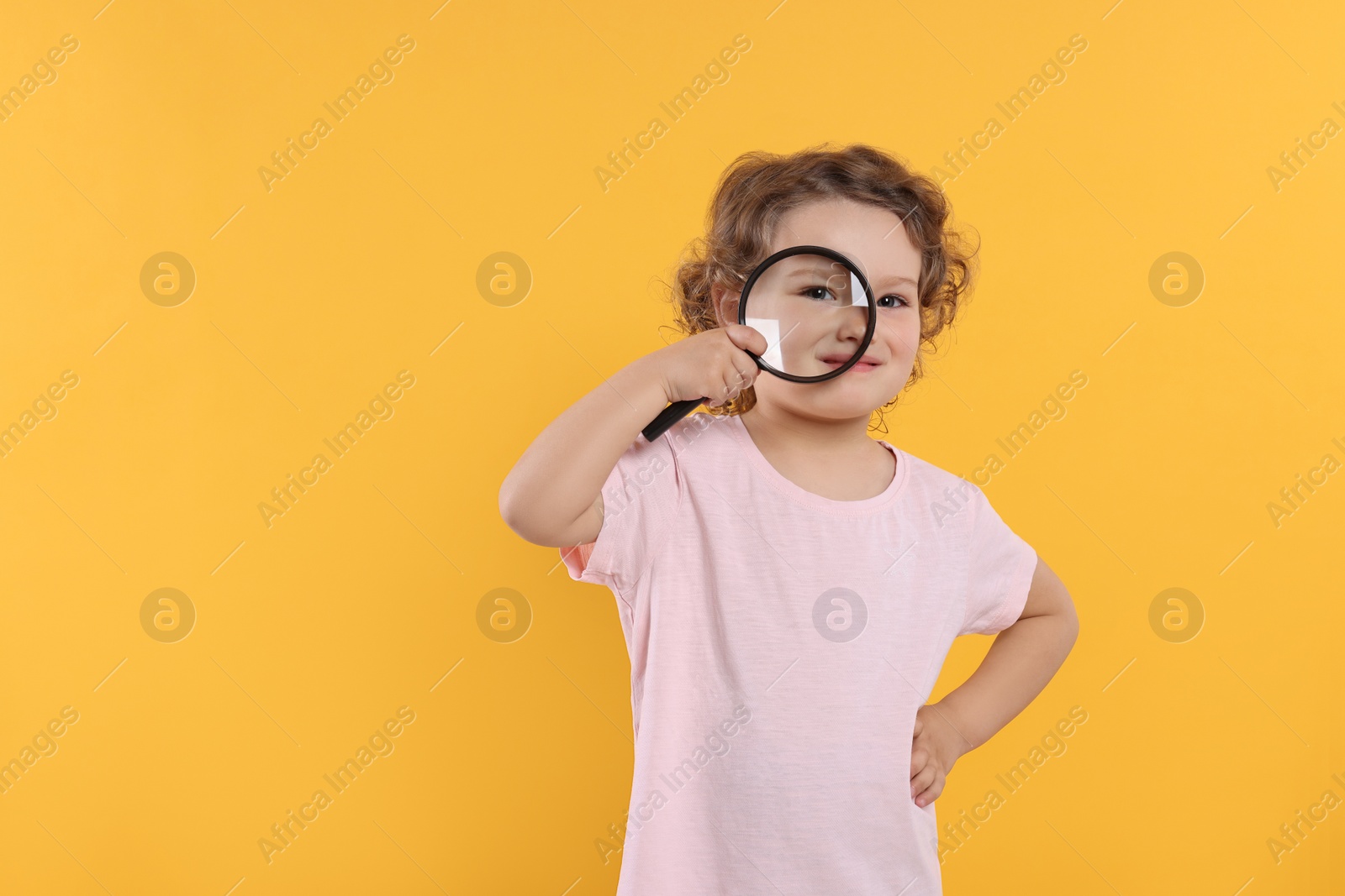Photo of Cute little girl looking through magnifier glass on orange background, space for text. Searching concept