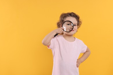 Cute little girl looking through magnifier glass on orange background, space for text. Searching concept