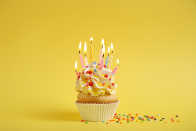 Birthday cupcake with burning candles on yellow background