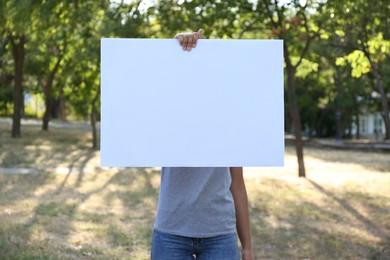 Woman holding blank poster outdoors. Mockup for design