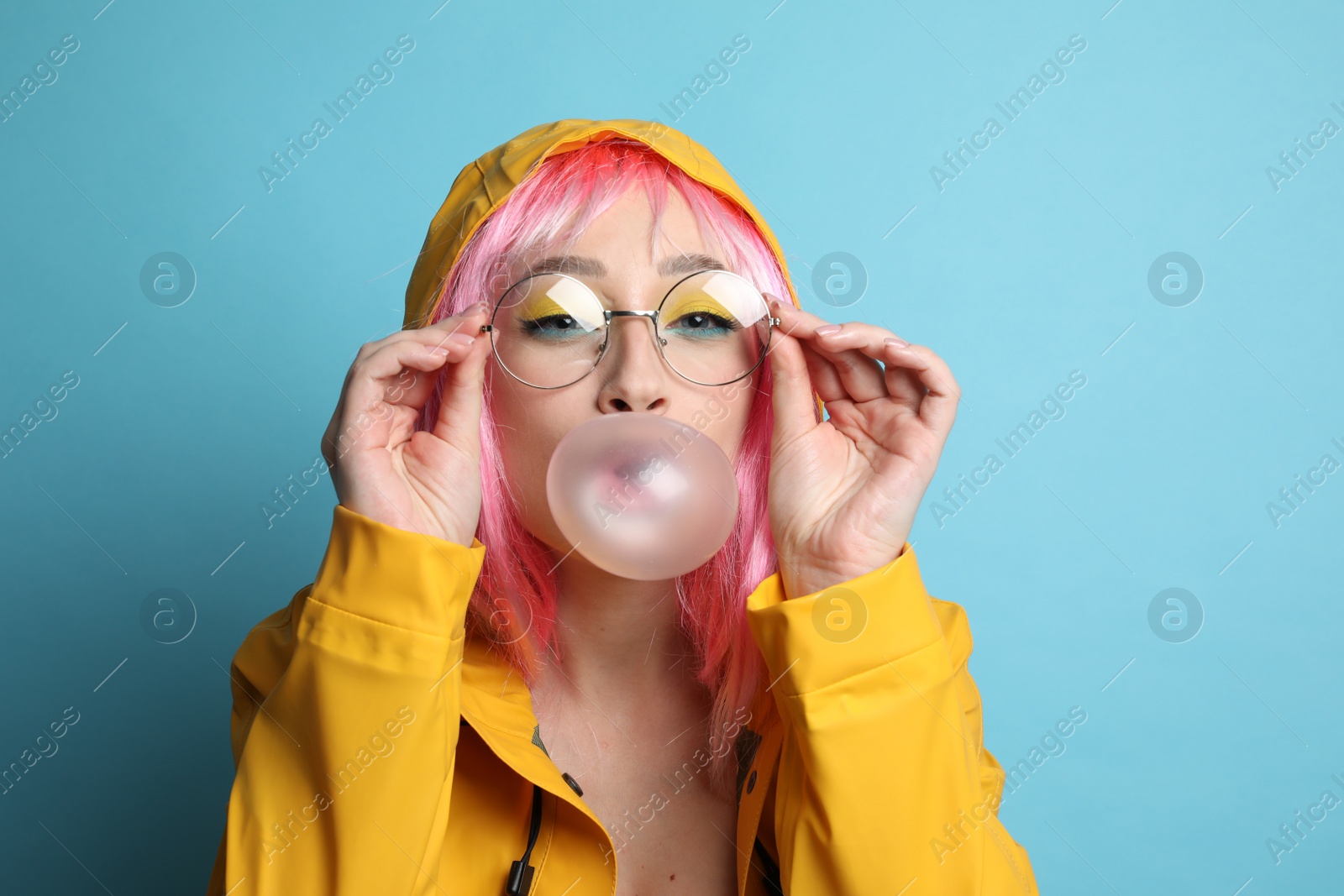 Photo of Fashionable young woman in pink wig with bright makeup blowing bubblegum on yellow background