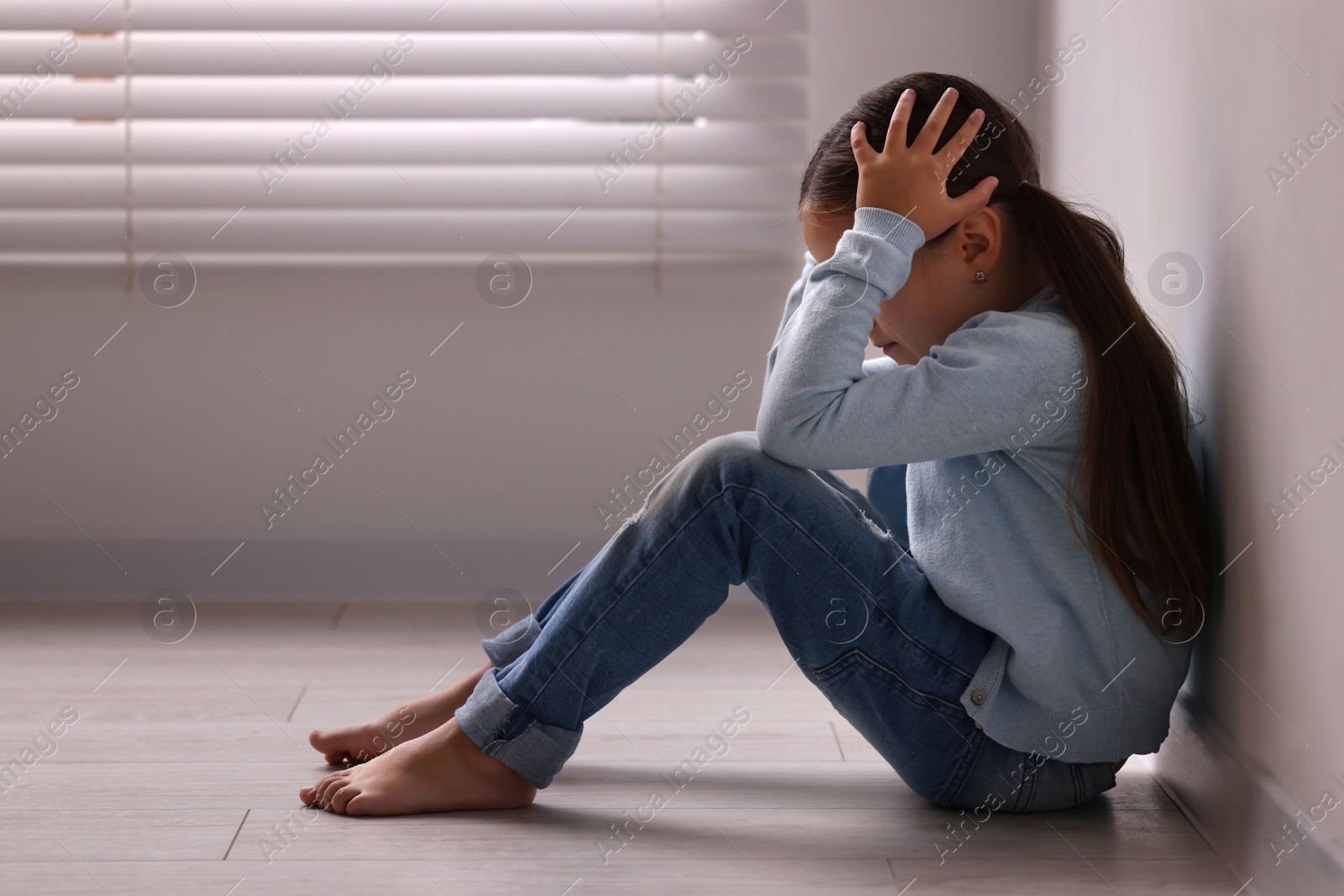 Photo of Child abuse. Upset little girl sitting on floor near light wall indoors