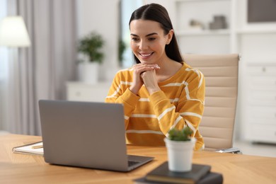 Photo of Young woman watching webinar at table in room