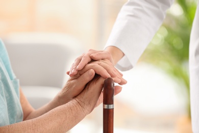 Nurse comforting elderly woman with cane against blurred background, closeup. Assisting senior generation