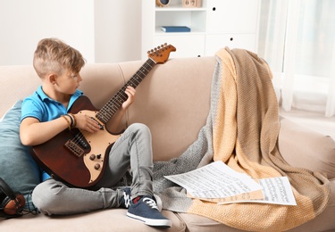 Photo of Cute little boy playing guitar on sofa in room. Space for text