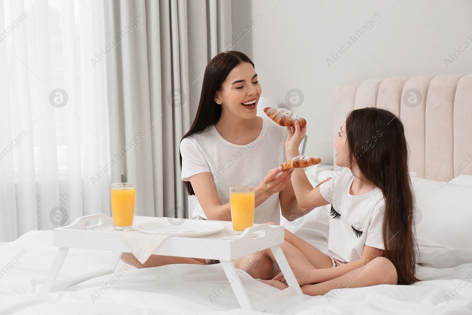 Photo of Young mother and her daughter having breakfast on bed at home