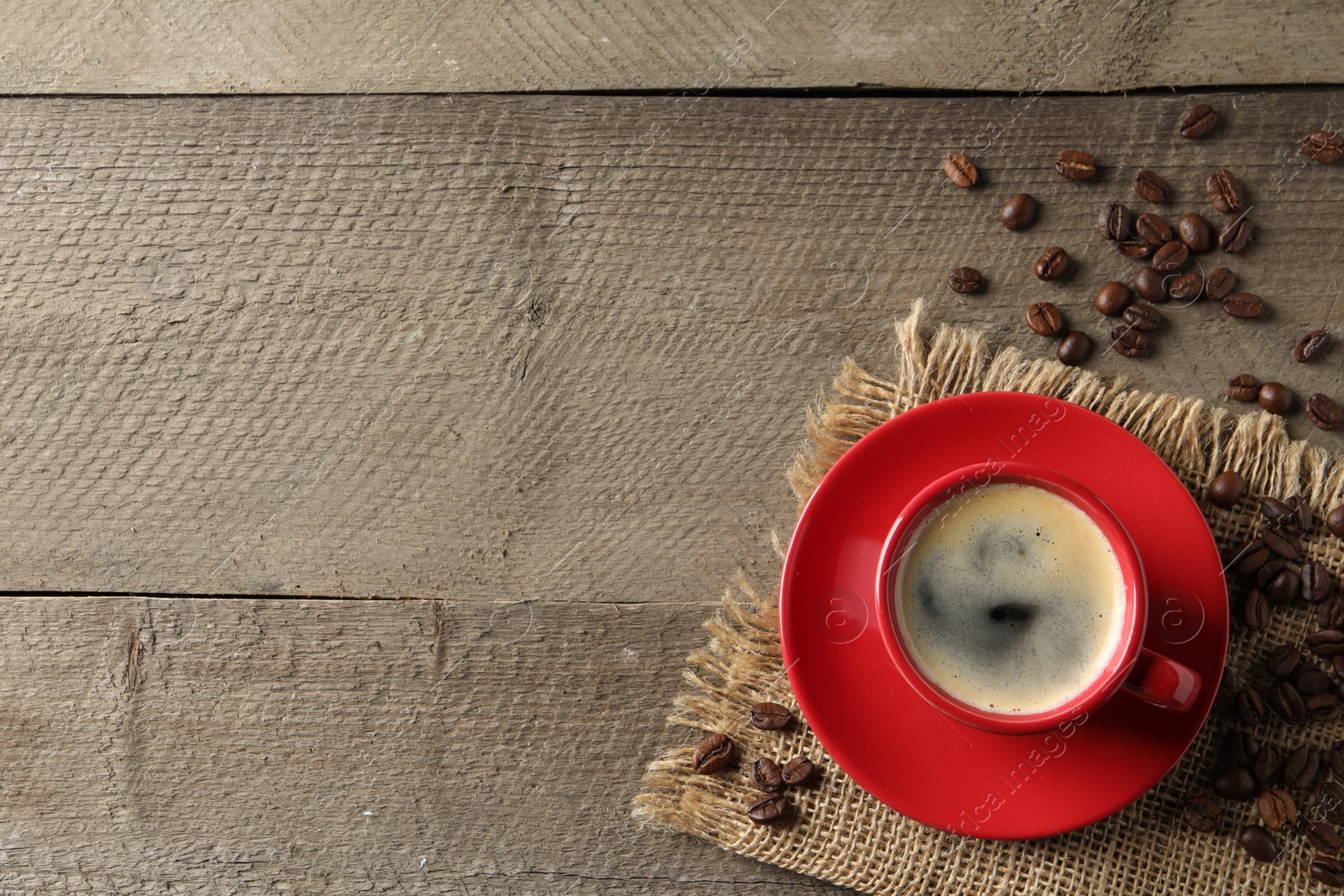 Photo of Cup of aromatic coffee and beans on wooden table, top view. Space for text