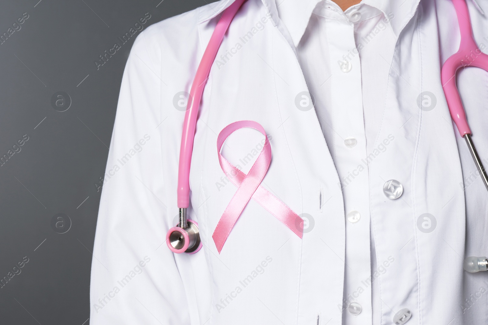 Photo of Female doctor with pink ribbon and stethoscope on grey background, closeup. Breast cancer concept