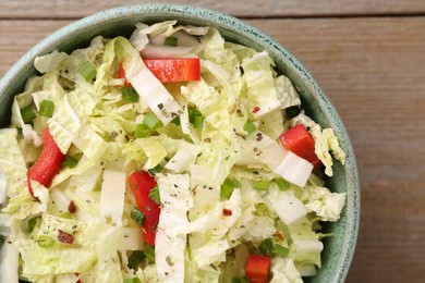 Tasty salad with Chinese cabbage, bell pepper and green onion in bowl on wooden table, top view