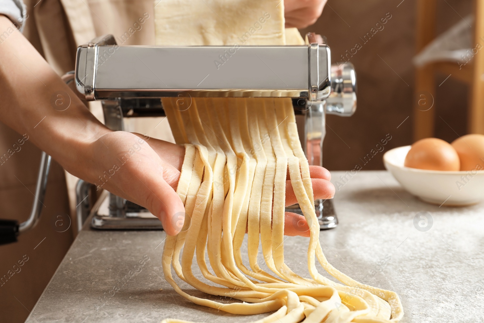 Photo of Young woman preparing noodles with pasta maker at table