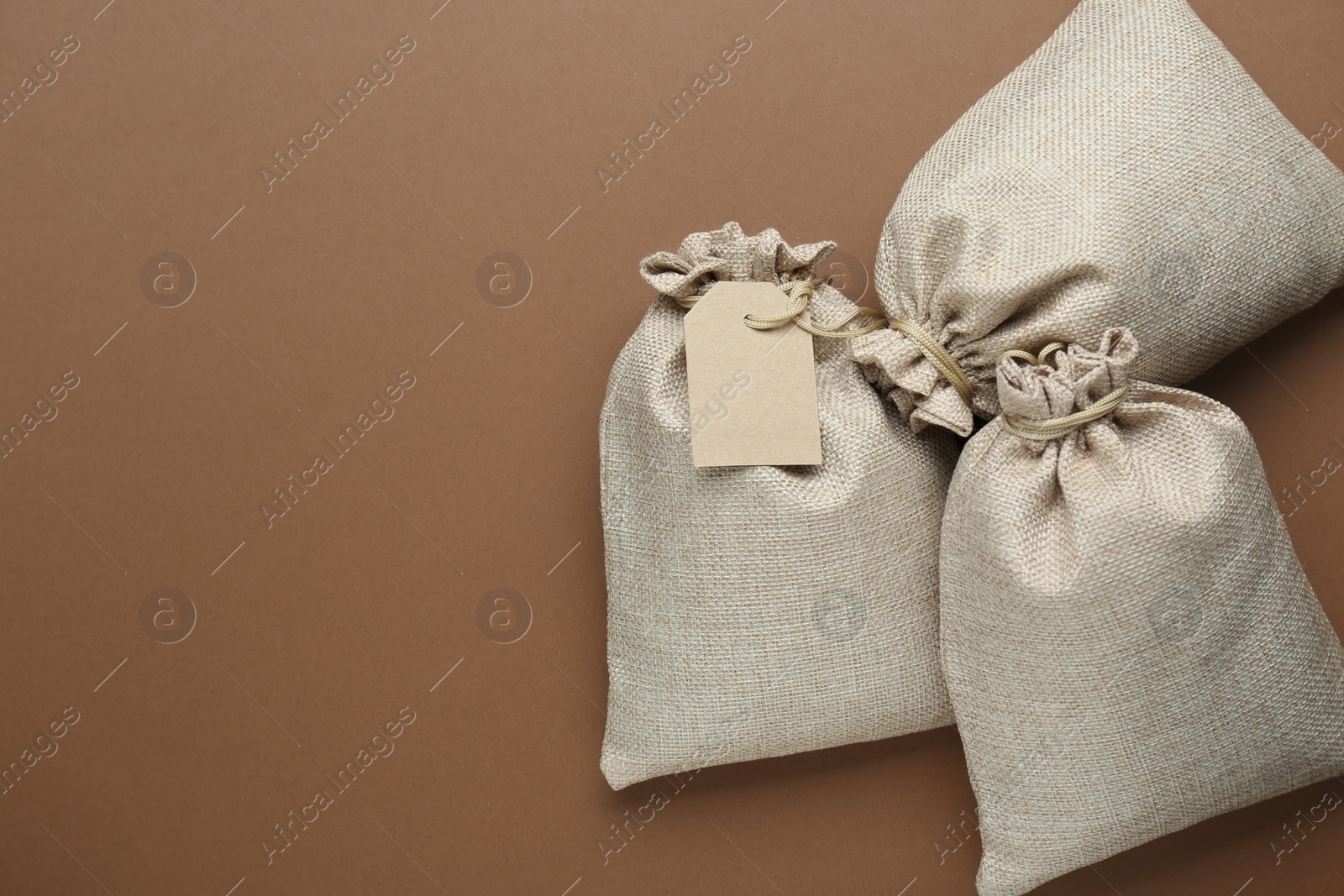 Photo of Tied burlap bags on brown background, flat lay. Space for text