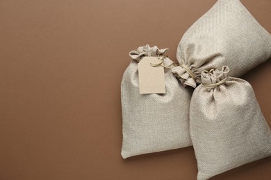 Photo of Tied burlap bags on brown background, flat lay. Space for text