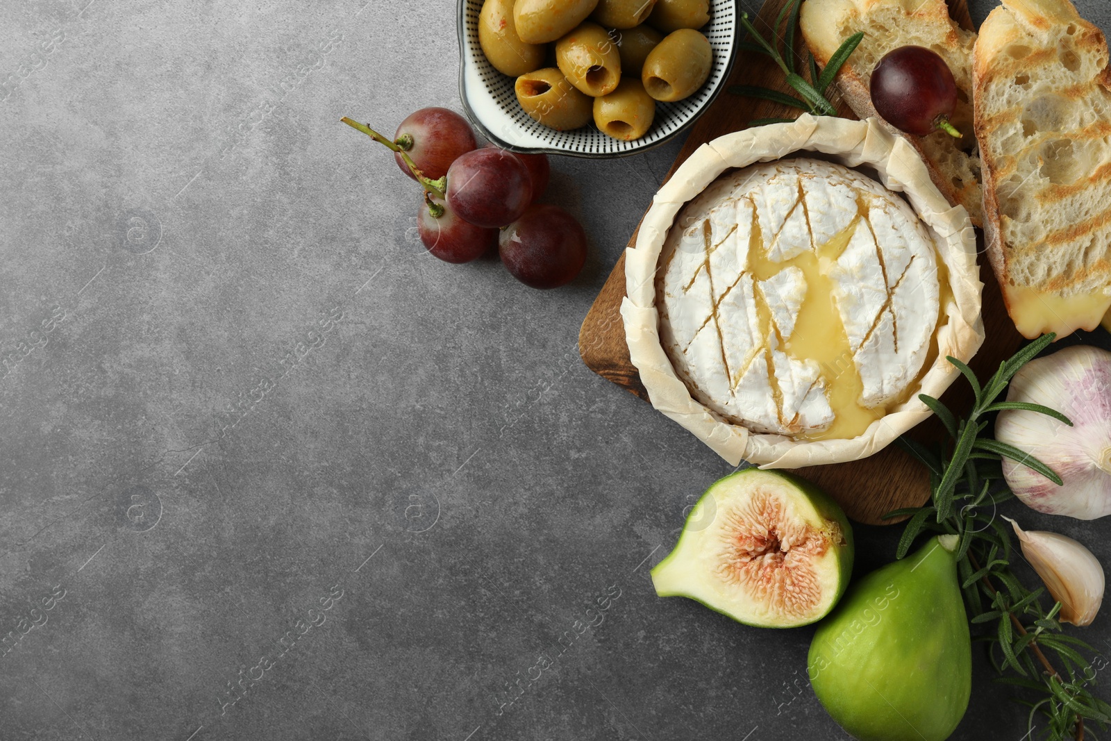 Photo of Tasty baked brie cheese and products on grey table, flat lay. Space for text