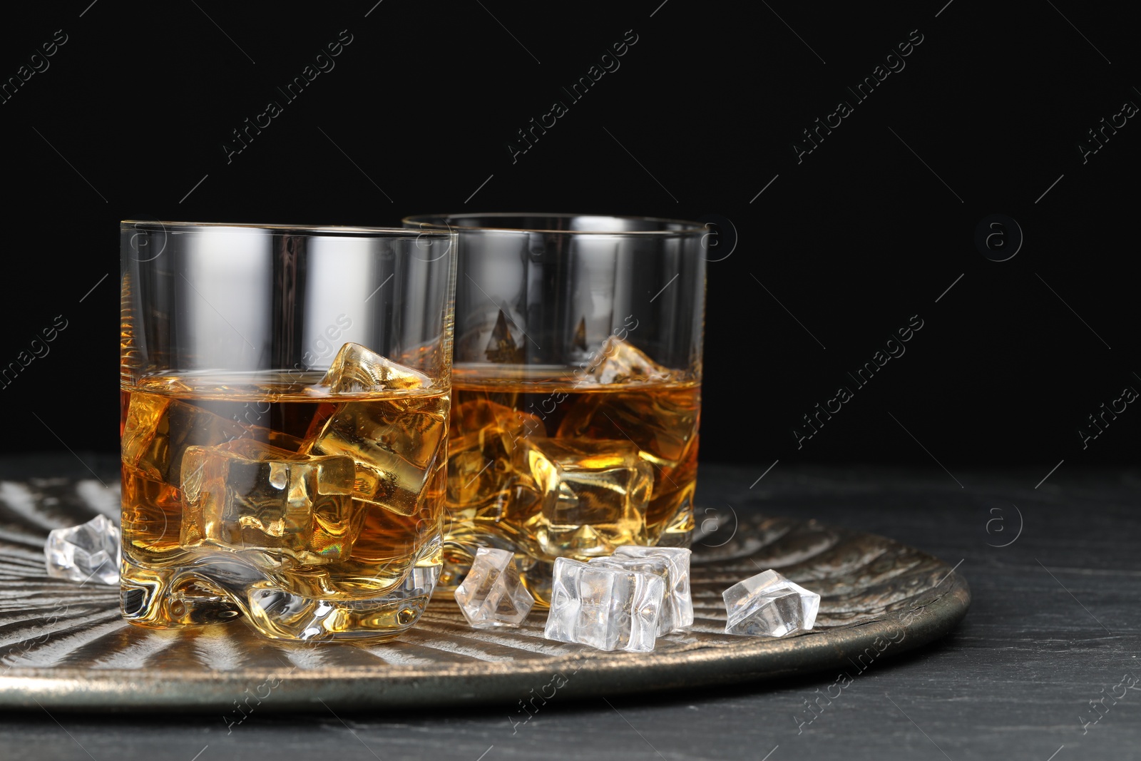 Photo of Whiskey and ice cubes in glasses on black table, closeup. Space for text