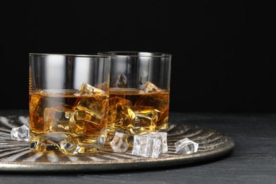 Photo of Whiskey and ice cubes in glasses on black table, closeup. Space for text