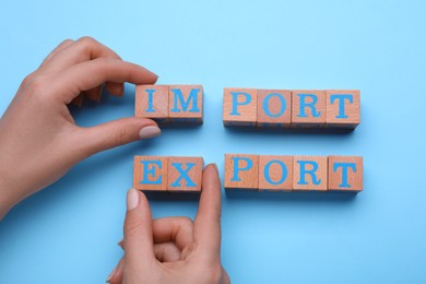 Photo of Woman making words Import and Export with wooden cubes on light blue background, top view