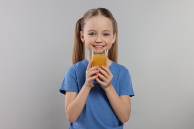 Cute little girl with glass of fresh juice on light gray background