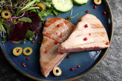 Photo of Pieces of delicious tuna with olives, salad and spices on black table, top view