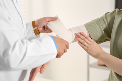 Photo of Orthopedist applying bandage onto patient's elbow in clinic, closeup