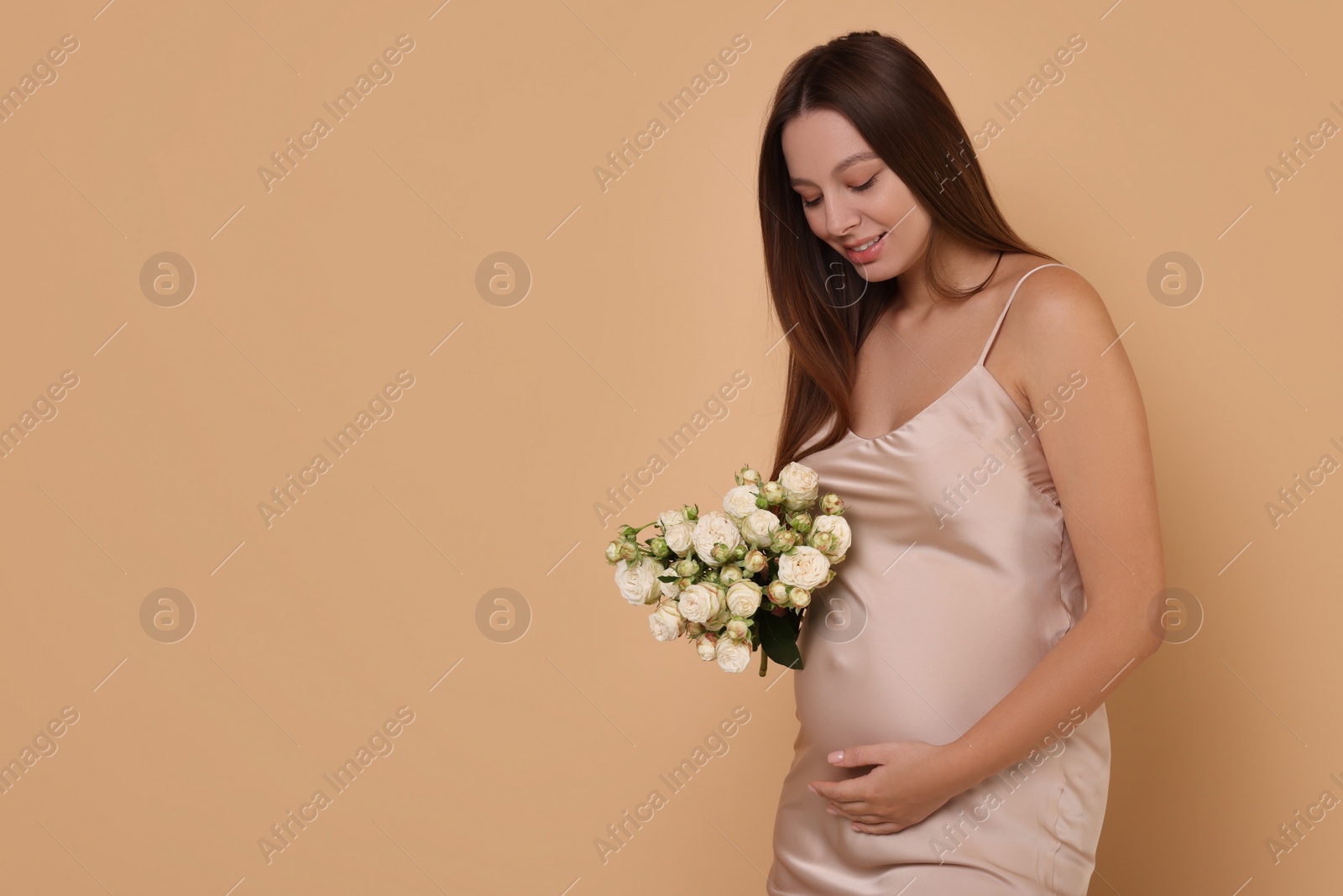 Photo of Beautiful pregnant woman in dress with bouquet of roses on beige background, space for text