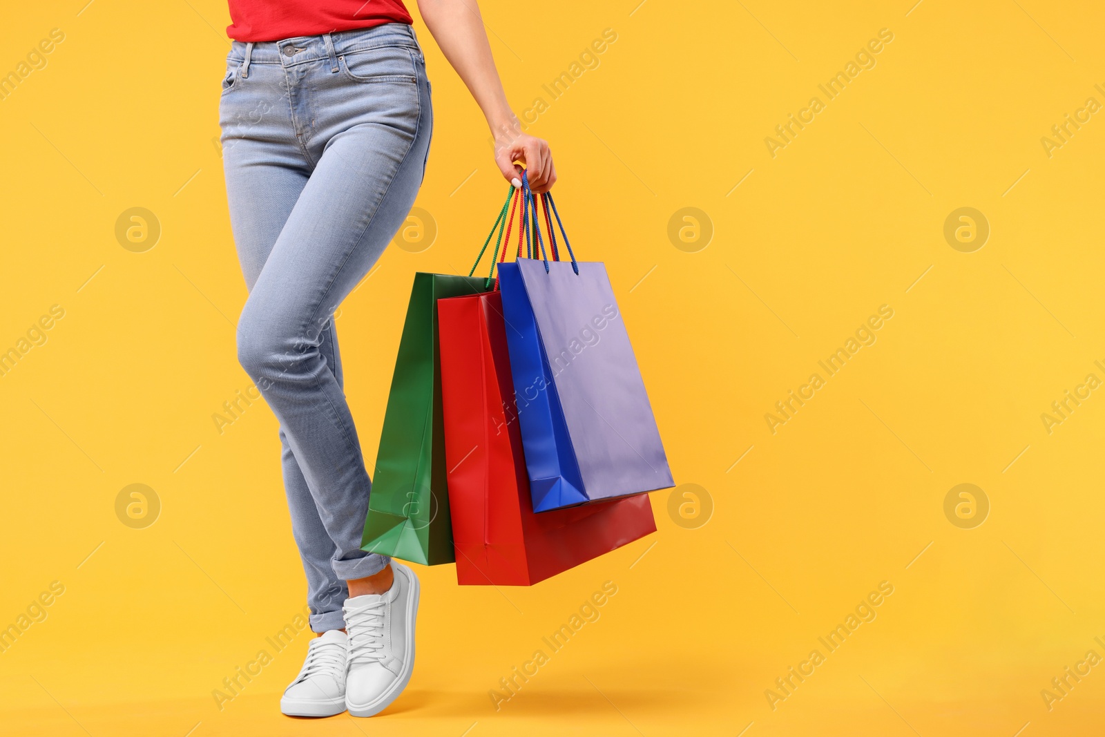 Photo of Woman with shopping bags on yellow background, closeup. Space for text