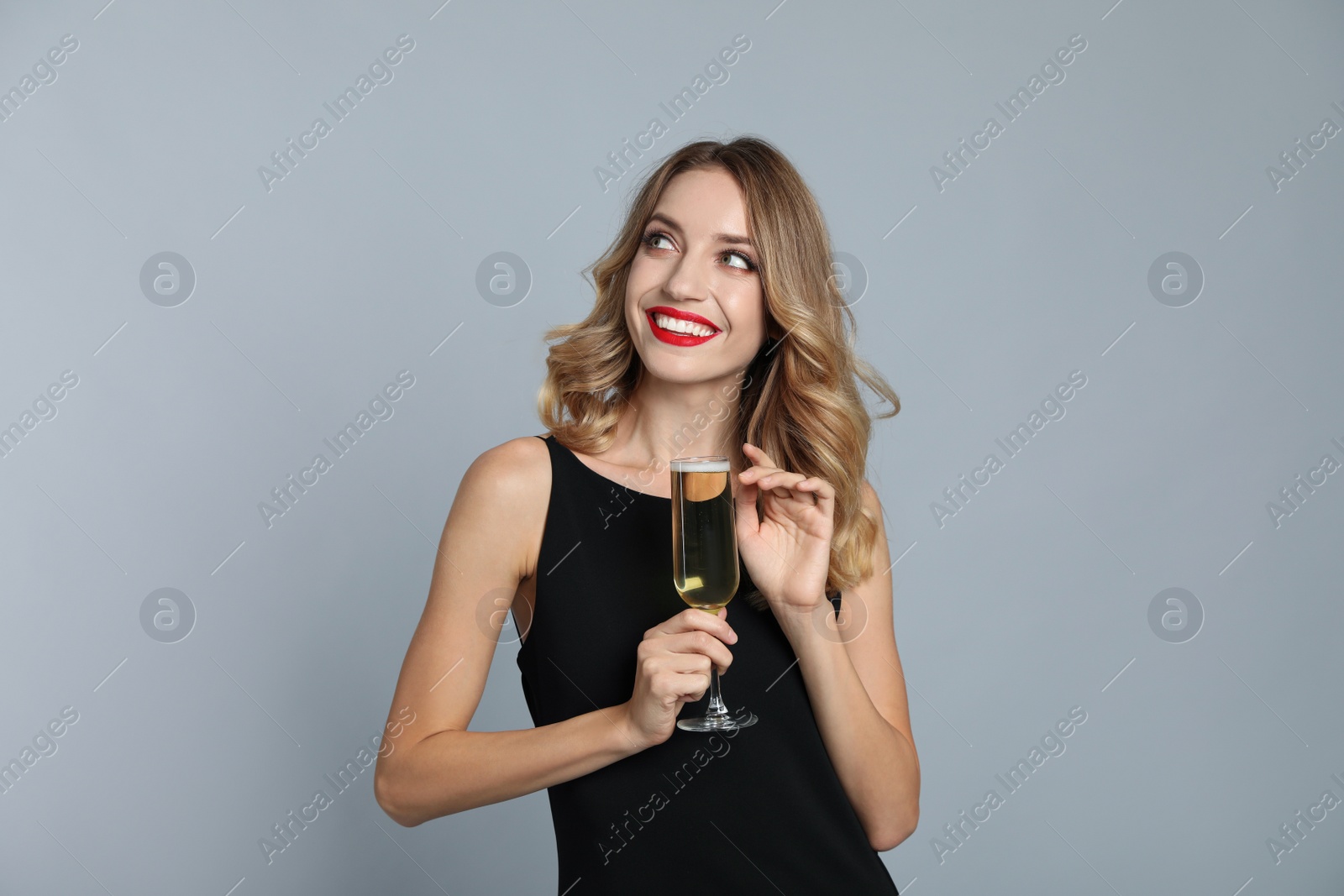 Photo of Happy young woman with glass of champagne on grey background. Christmas celebration