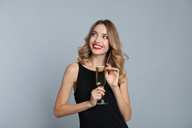 Happy young woman with glass of champagne on grey background. Christmas celebration