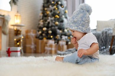 Photo of Little baby with knitted hat and Christmas ball on floor at home