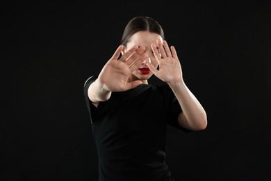 Photo of Beautiful woman covering face with hands on black background