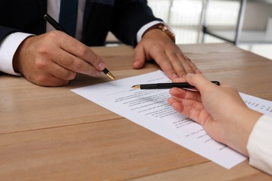 Businesspeople working with contract at wooden table indoors, closeup