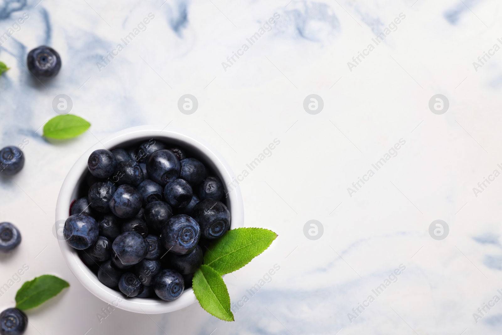 Photo of Tasty fresh bilberries and green leaves in bowl on white table, flat lay. Space for text