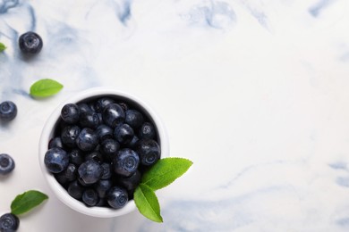 Tasty fresh bilberries and green leaves in bowl on white table, flat lay. Space for text