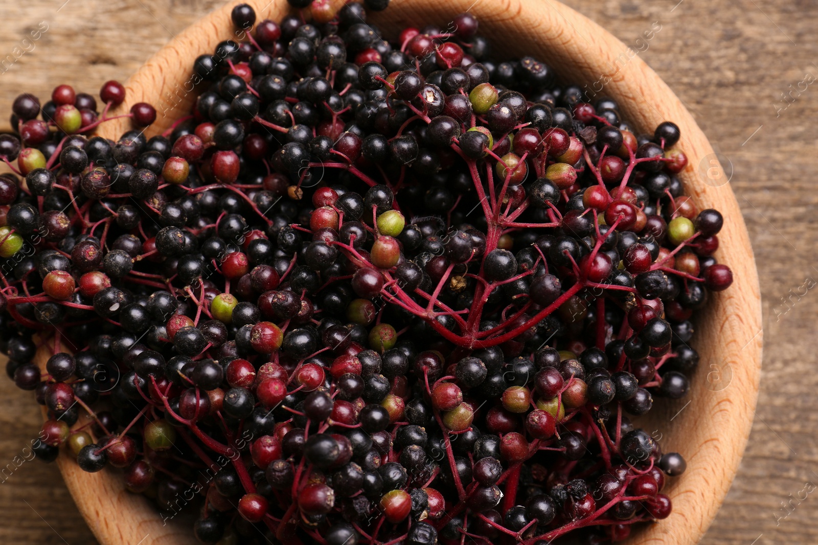 Photo of Bowl with tasty elderberries (Sambucus) on wooden table, top view