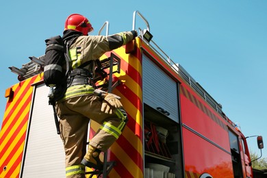 Firefighter in uniform on fire truck outdoors, back view