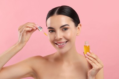 Beautiful young woman applying serum onto her face on pink background