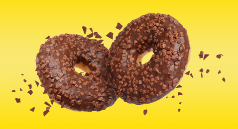 Sweet delicious donuts falling on yellow background