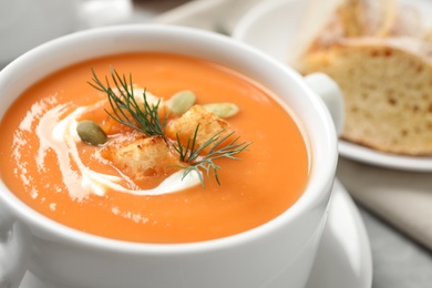 Photo of Tasty creamy pumpkin soup with croutons, seeds and dill in bowl on table, closeup