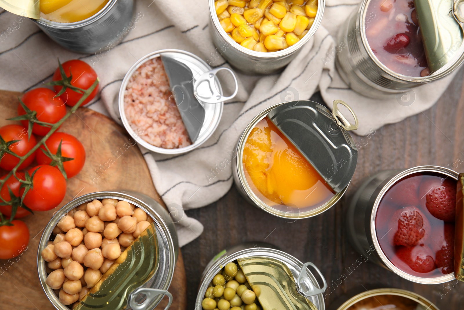 Photo of Open tin cans with different products on wooden table, flat lay