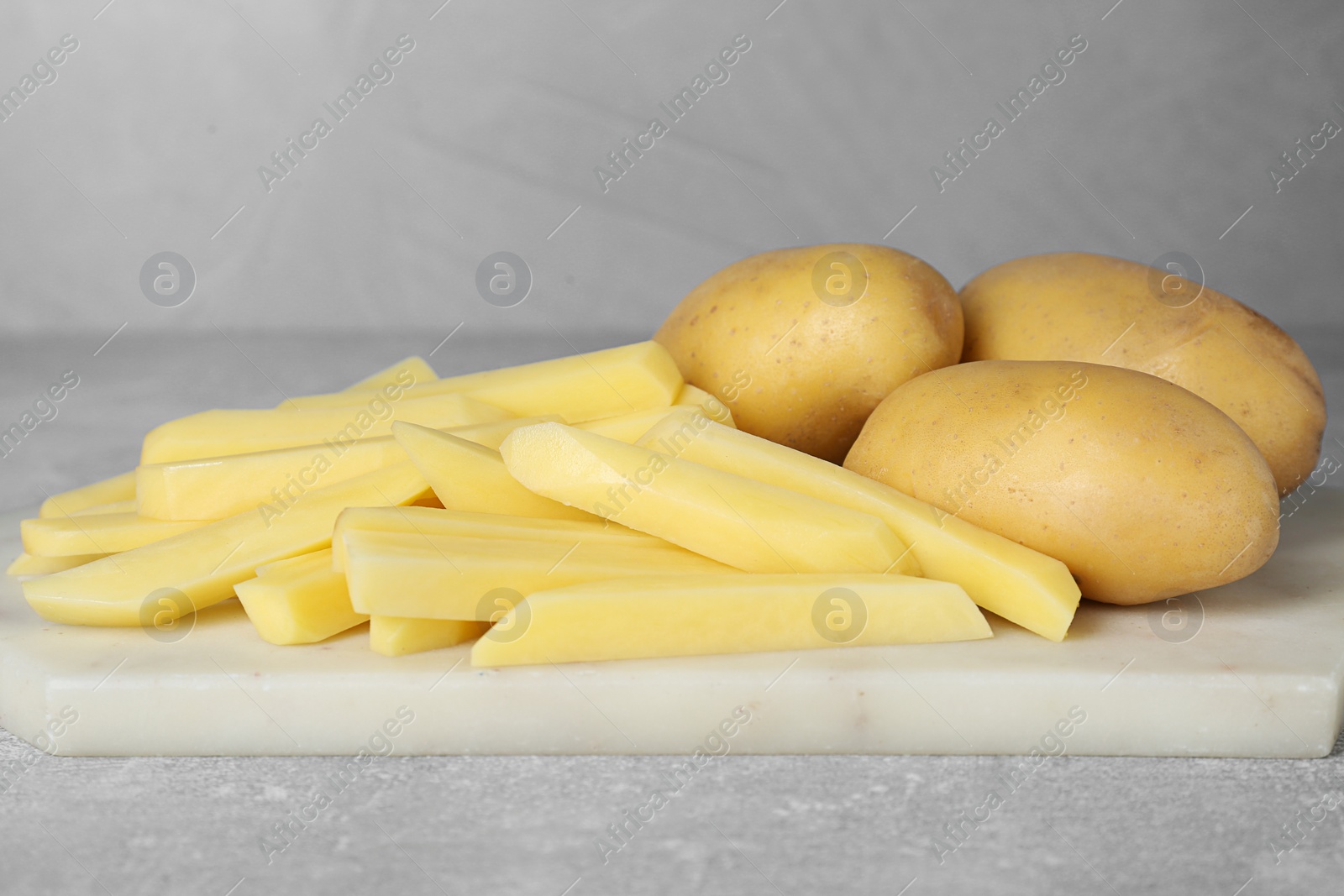 Photo of Whole and cut raw potatoes on light grey table, closeup. Cooking delicious French fries