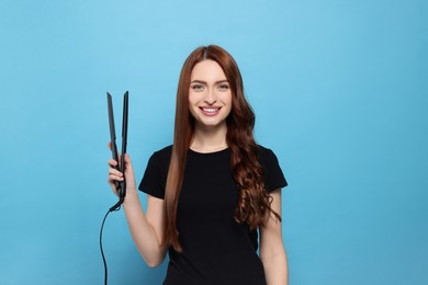 Beautiful woman with hair iron on light blue background